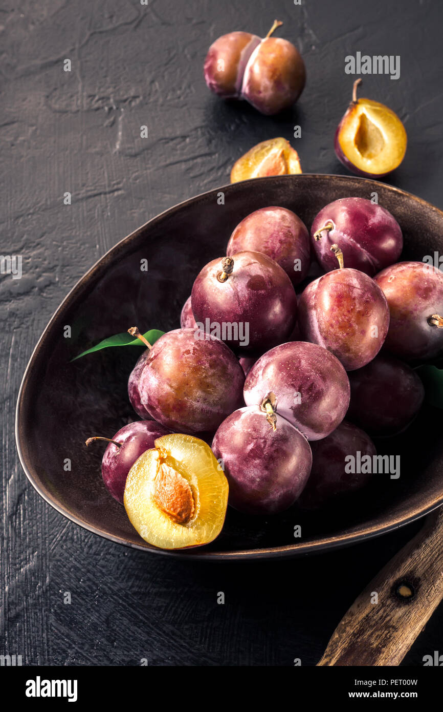 Fruits rouges frais entier bleu-violet, prunes et couper des tranches avec un couteau dans un bol sur une table de cuisine Concept de confiture maison cuisine compote n par sa propre main Banque D'Images