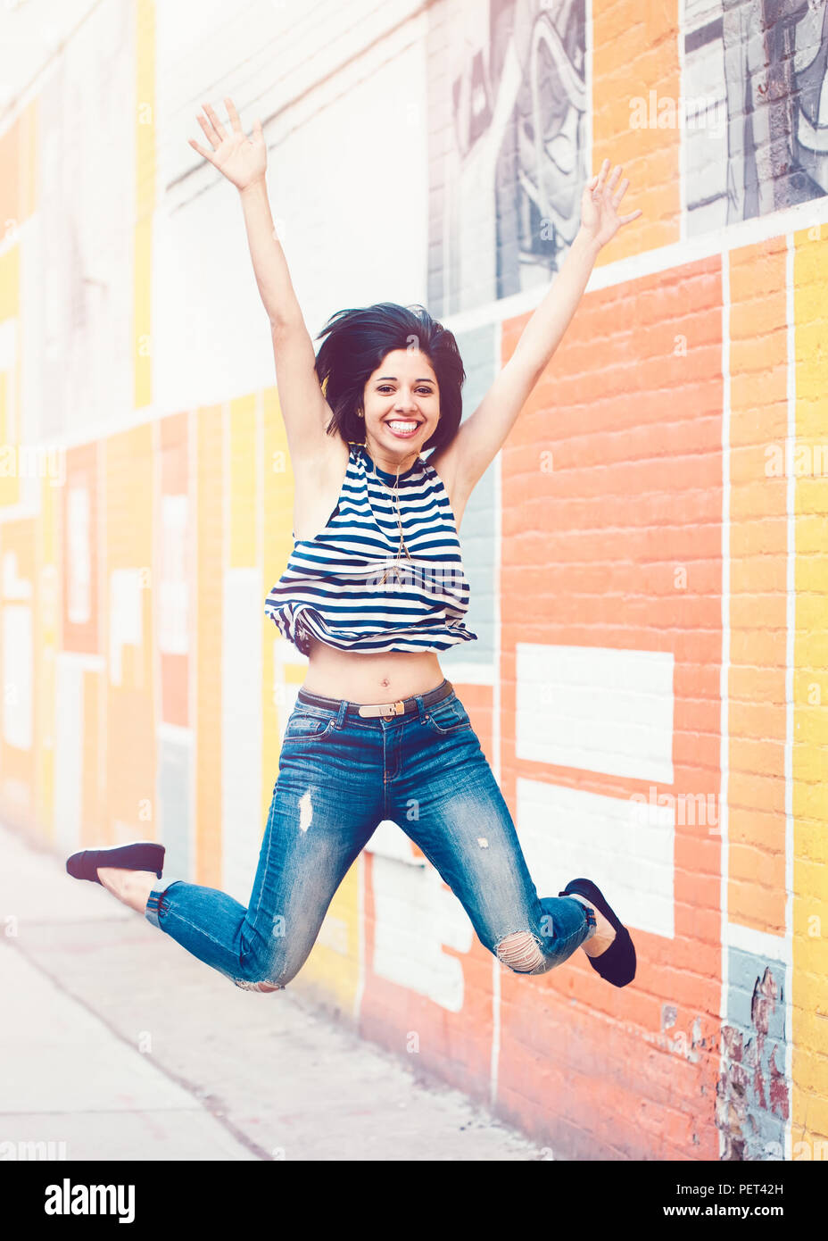 Portrait of beautiful smiling laughing young hispanic latin hipster femme en bleu jeans, T-shirt à rayures, sauter de haut dans l'air en ville à la recherche de ca Banque D'Images
