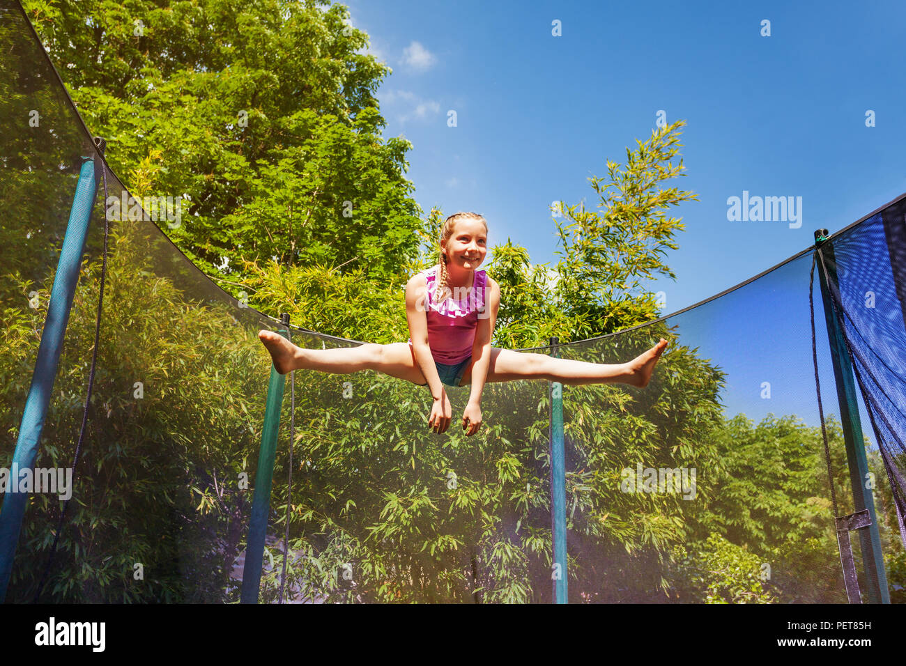 Portrait à angle faible de preteen girl effectuant un saut split dans l'air, l'exercice sur le trampoline à l'extérieur Banque D'Images