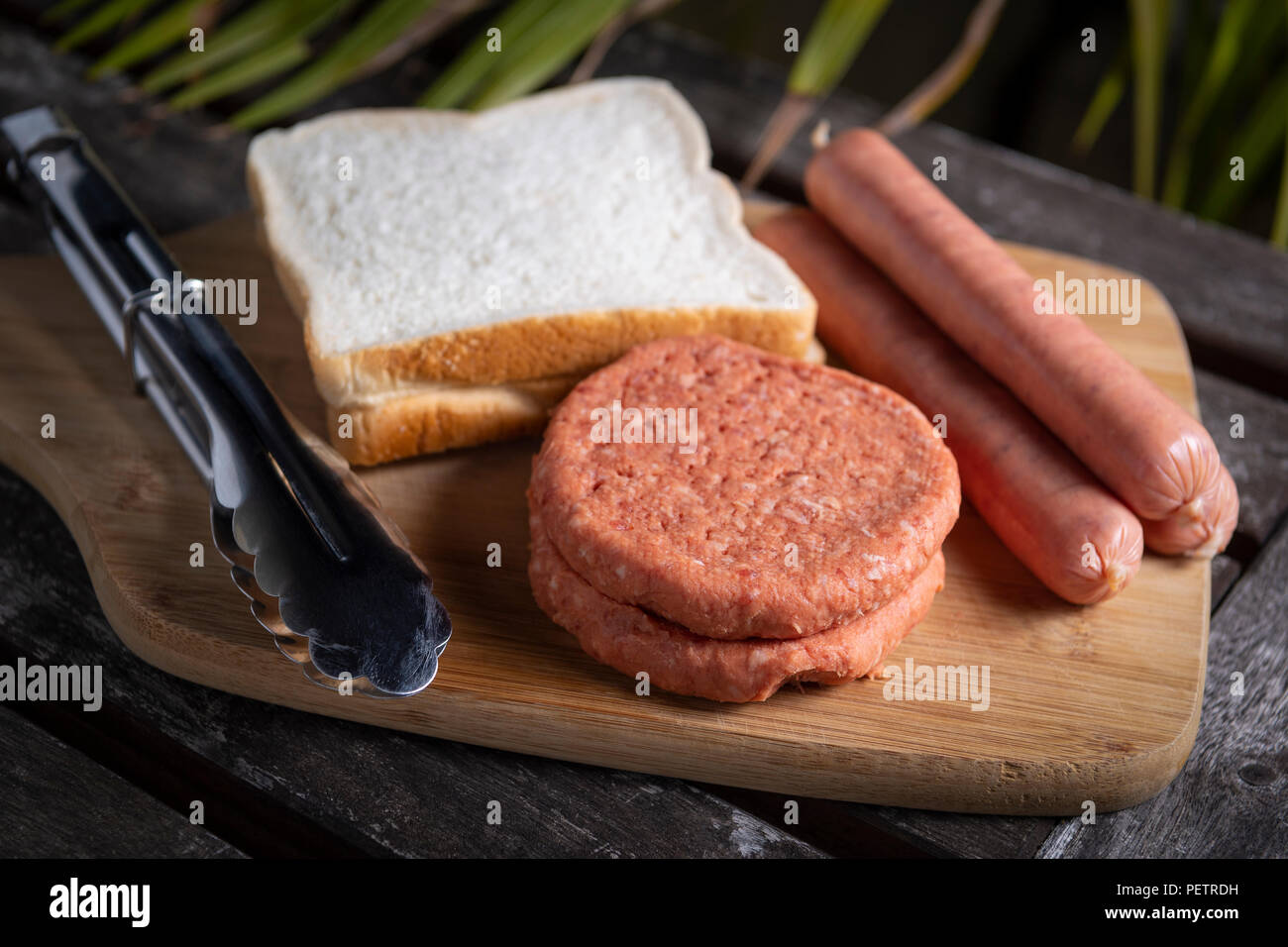 Saucisses barbecue non cuites fraîches, des hamburgers et du pain prêt à être grillé, sur la planche à découper en bois Banque D'Images