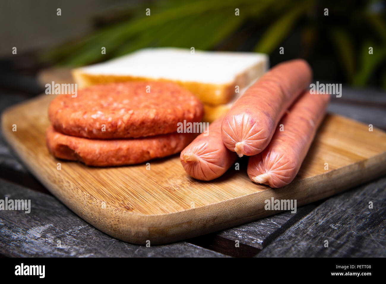 Saucisses barbecue non cuites fraîches, des hamburgers et du pain prêt à être grillé, sur la planche à découper en bois Banque D'Images