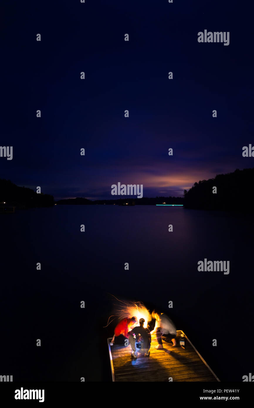 Un groupe d'amis d'artifice éclairage éteint sur un quai au bord du lac la nuit. Banque D'Images