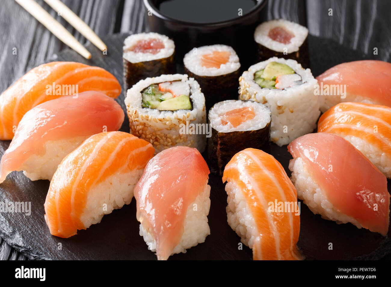 Des sushis fraîchement préparés avec le saumon et le thon, California rolls, maki avec de la sauce soja, baguettes close-up sur l'ardoise noire sur la table du Conseil. Banque D'Images
