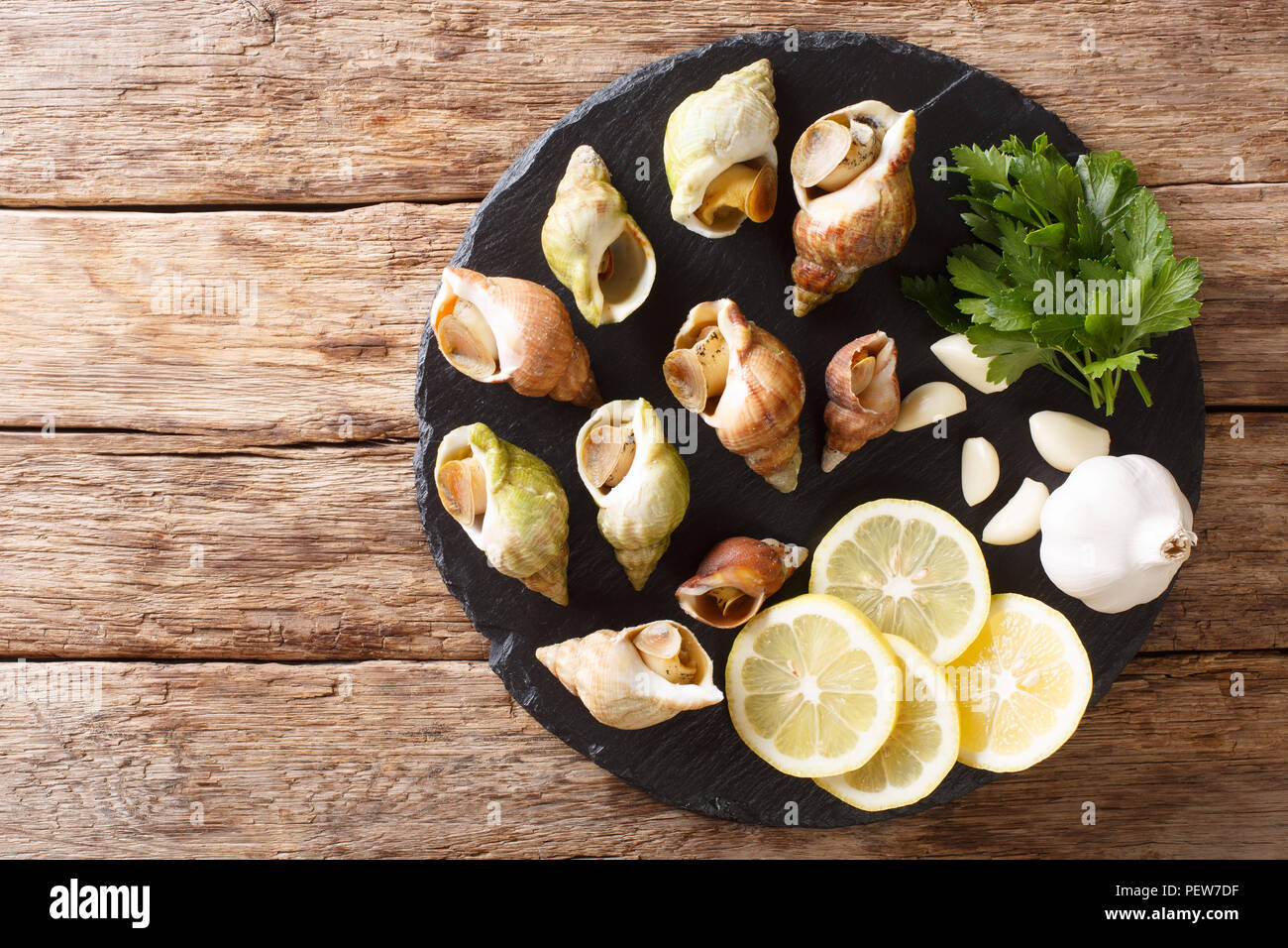 Buccinum undatum buccin commun, les escargots de mer, avec un l'ail et persil, citron gros plan sur une table horizontale. haut Vue de dessus Banque D'Images