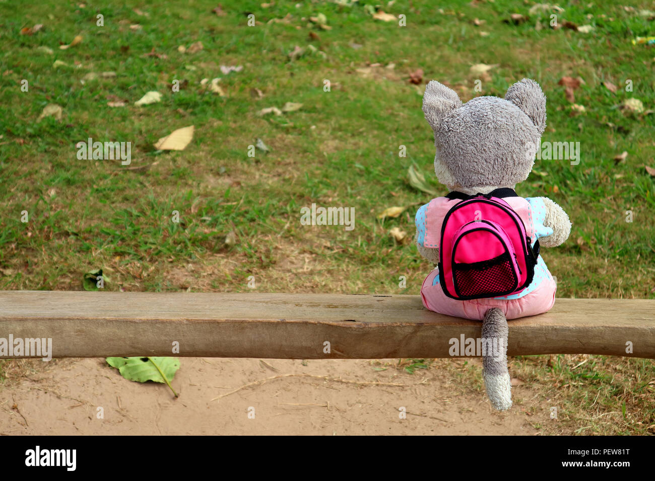Happy voyageur solo ! Un chiot mignon peluche rose vif avec sac à dos, assis sur un banc en bois dans le parc Banque D'Images