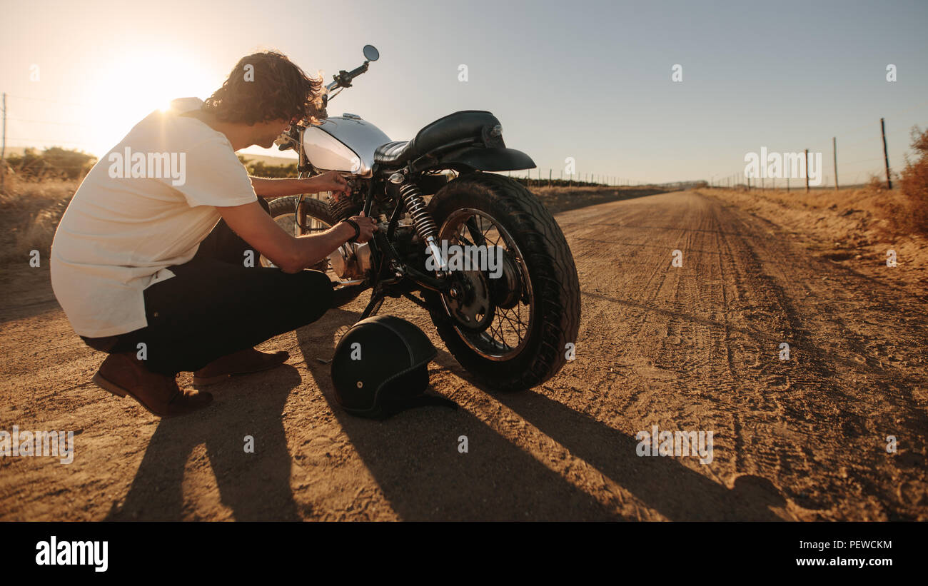 Jeune homme du tuyau de carburant contrôle de sa moto sur route de campagne. Réparer sa moto motard sur les routes rurales vide. Banque D'Images