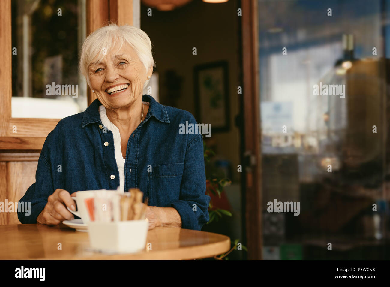 Portrait of smiling vieille femme assise au café avec une tasse de café sur la table. Belle senior woman at coffee shop à la caméra et au sourire. Banque D'Images