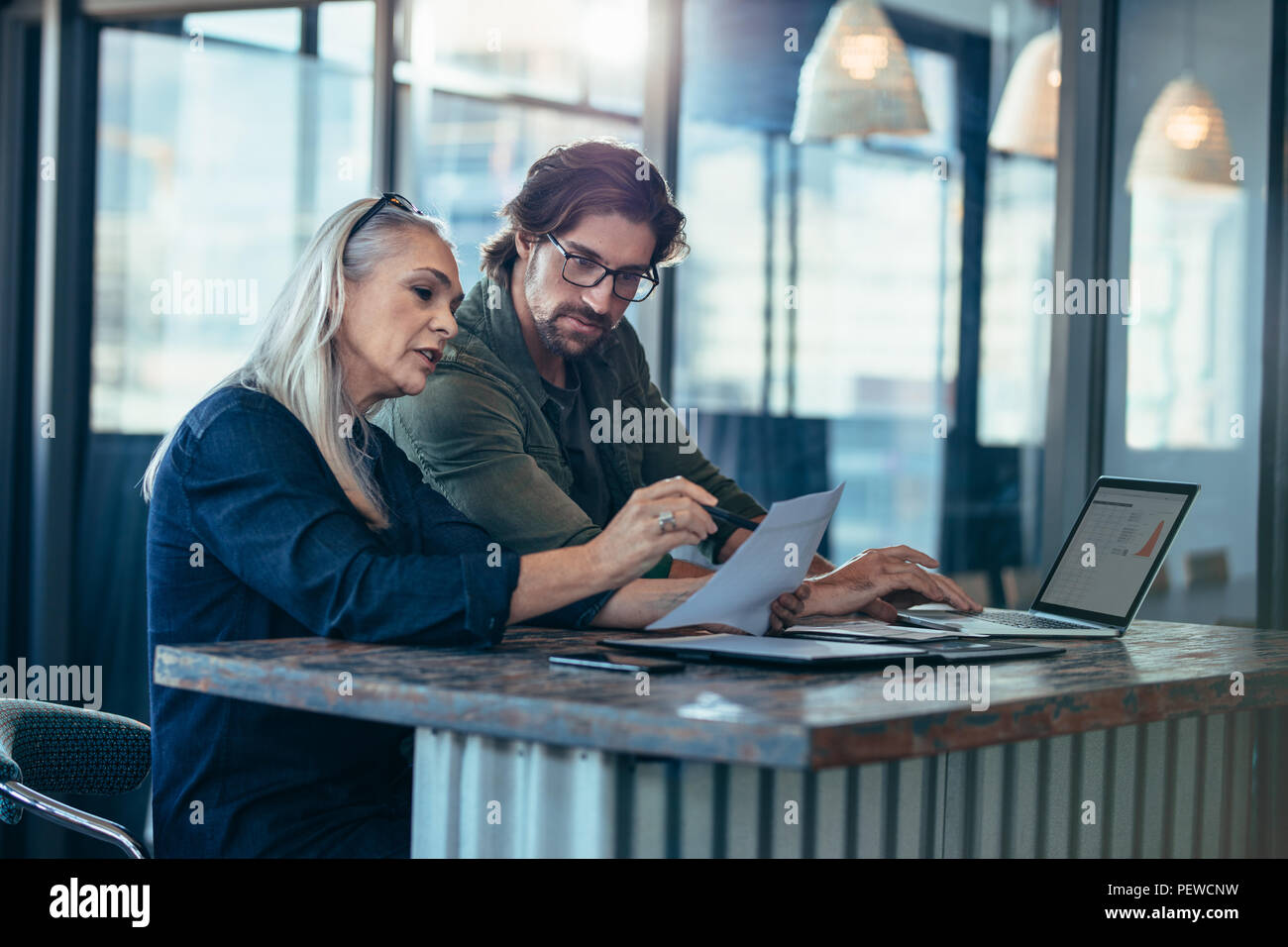 Senior woman discuter travail avec collègue masculin. Deux associés travaillent ensemble dans le bureau et de parler au cours d'un rapport. Banque D'Images