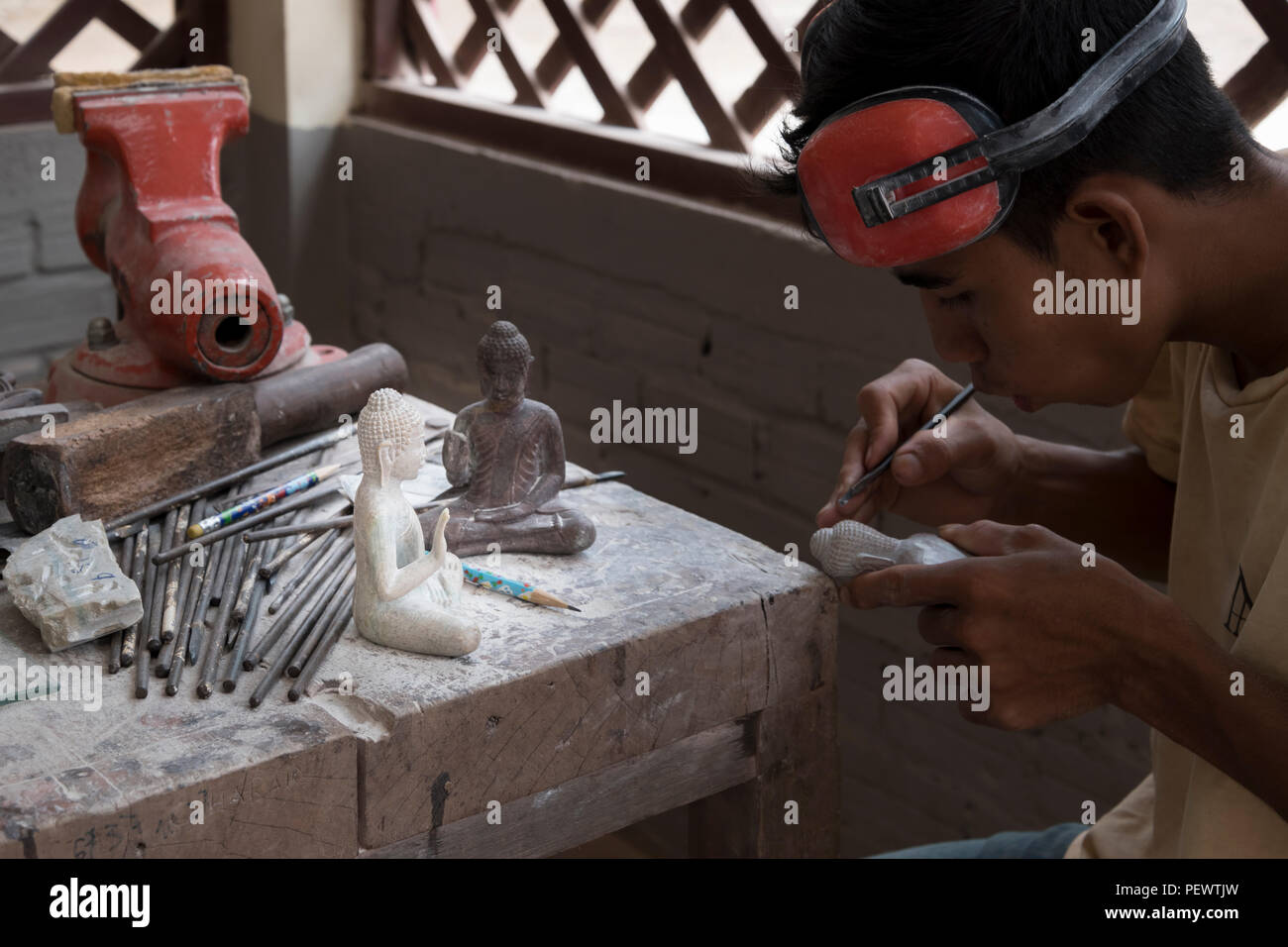 Un sculpteur cambodgien sculpte soigneusement un Bouddha en pierre dans un centre d'art de Siem Reap, reflétant l'artisanat traditionnel et la vie quotidienne en Asie. Banque D'Images