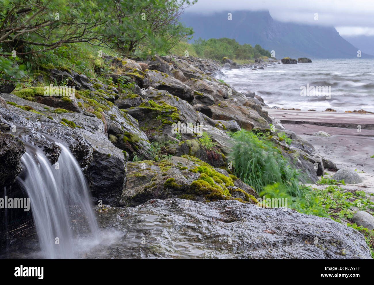 Peu de rigoles aux projections d'eau sur un rocher et en arrière-plan des nuages bas et des vagues de la mer, photo du nord de la Norvège. Banque D'Images