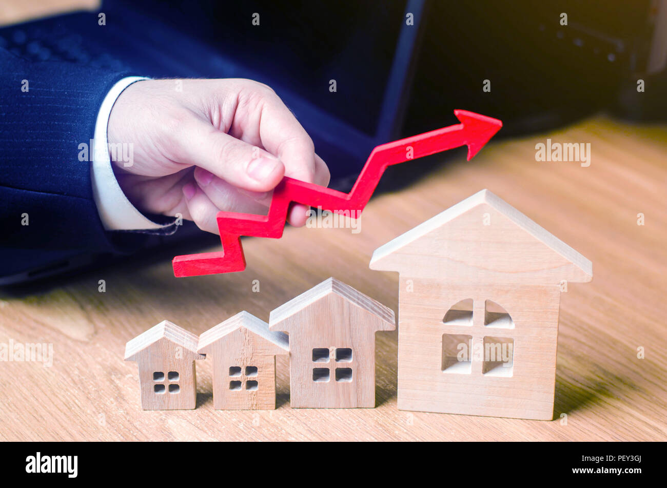 La main est titulaire d'une flèche rouge au-dessus des maisons en bois. Concept de l'augmentation de l'offre et la demande sur le marché immobilier. Augmentation du coût et pri Banque D'Images