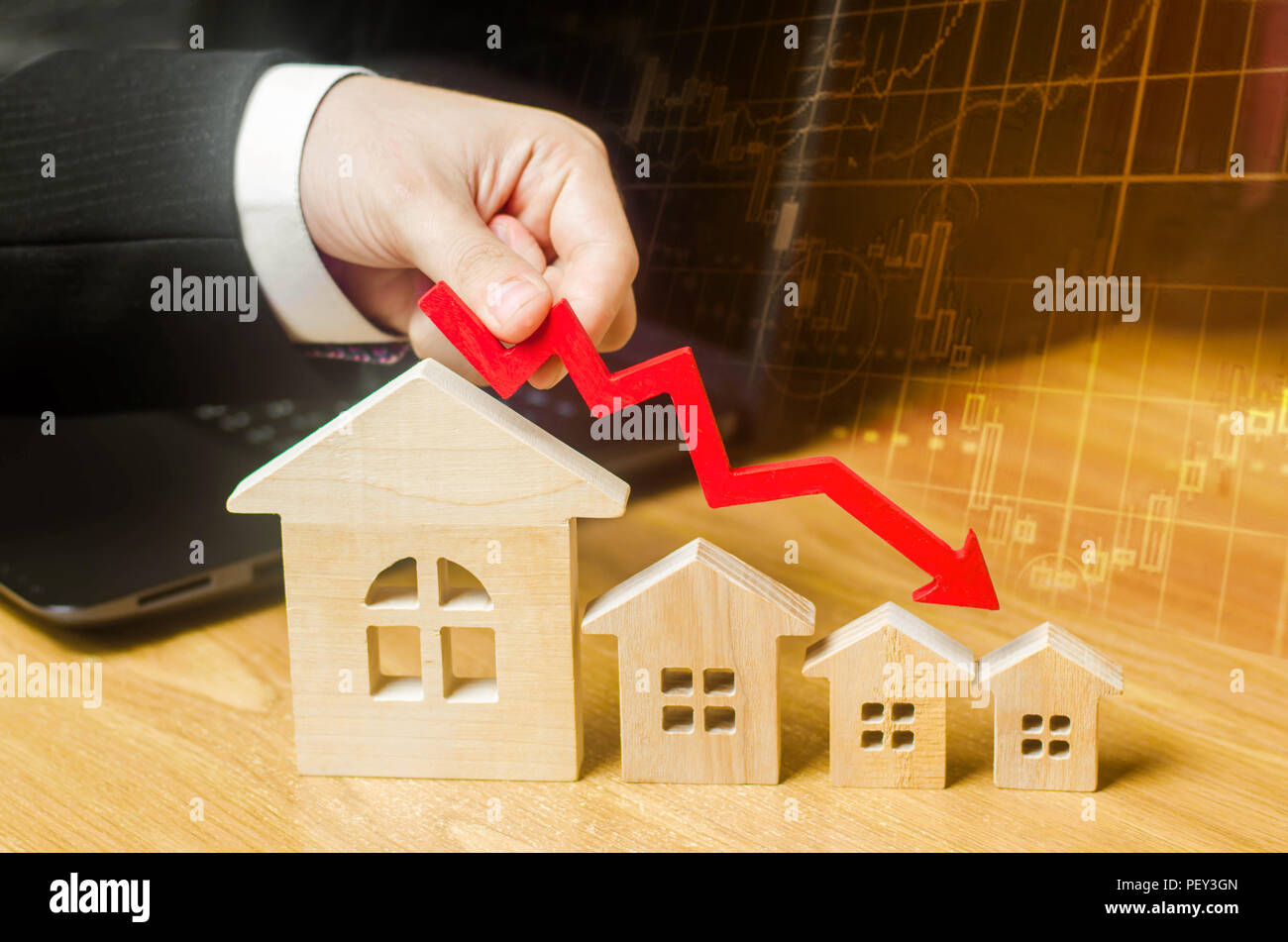 La main est titulaire d'une flèche rouge au-dessus des maisons en bois en bas. Les maisons sont en baisse. Le concept de la baisse de la demande et l'offre sur le marché de l'immobilier Banque D'Images