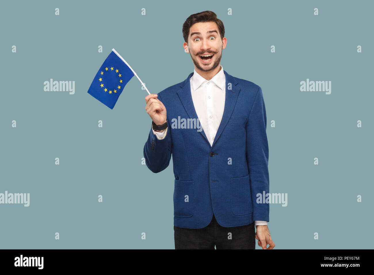 Temps pour l'Europe. Bel homme surpris en veste bleue et chemise blanche holding drapeau de l'Union européenne et à la caméra à se demande avec visage. L'Indo Banque D'Images