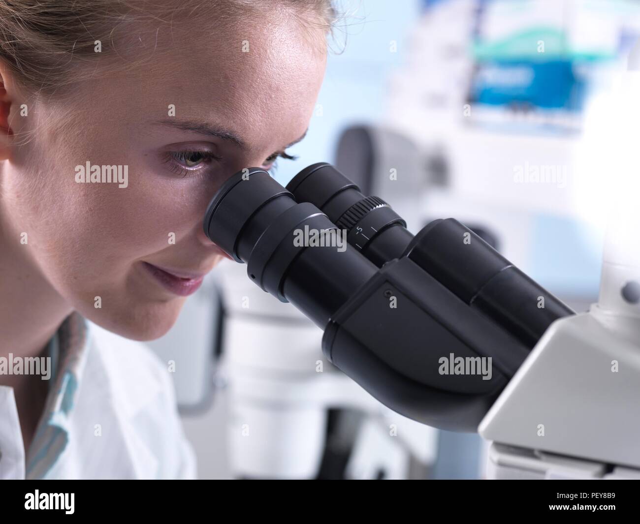 Les jeunes diplômés de sexe féminin de l'affichage d'un échantillon d'un microscope. Banque D'Images