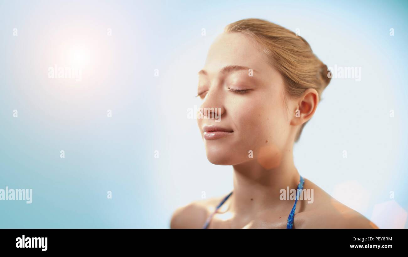 Femme dans la lumière du soleil avec les yeux fermés. Banque D'Images