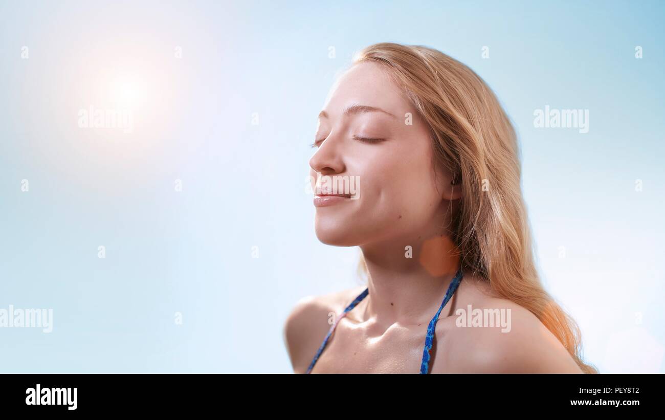 Femme dans la lumière du soleil avec les yeux fermés. Banque D'Images