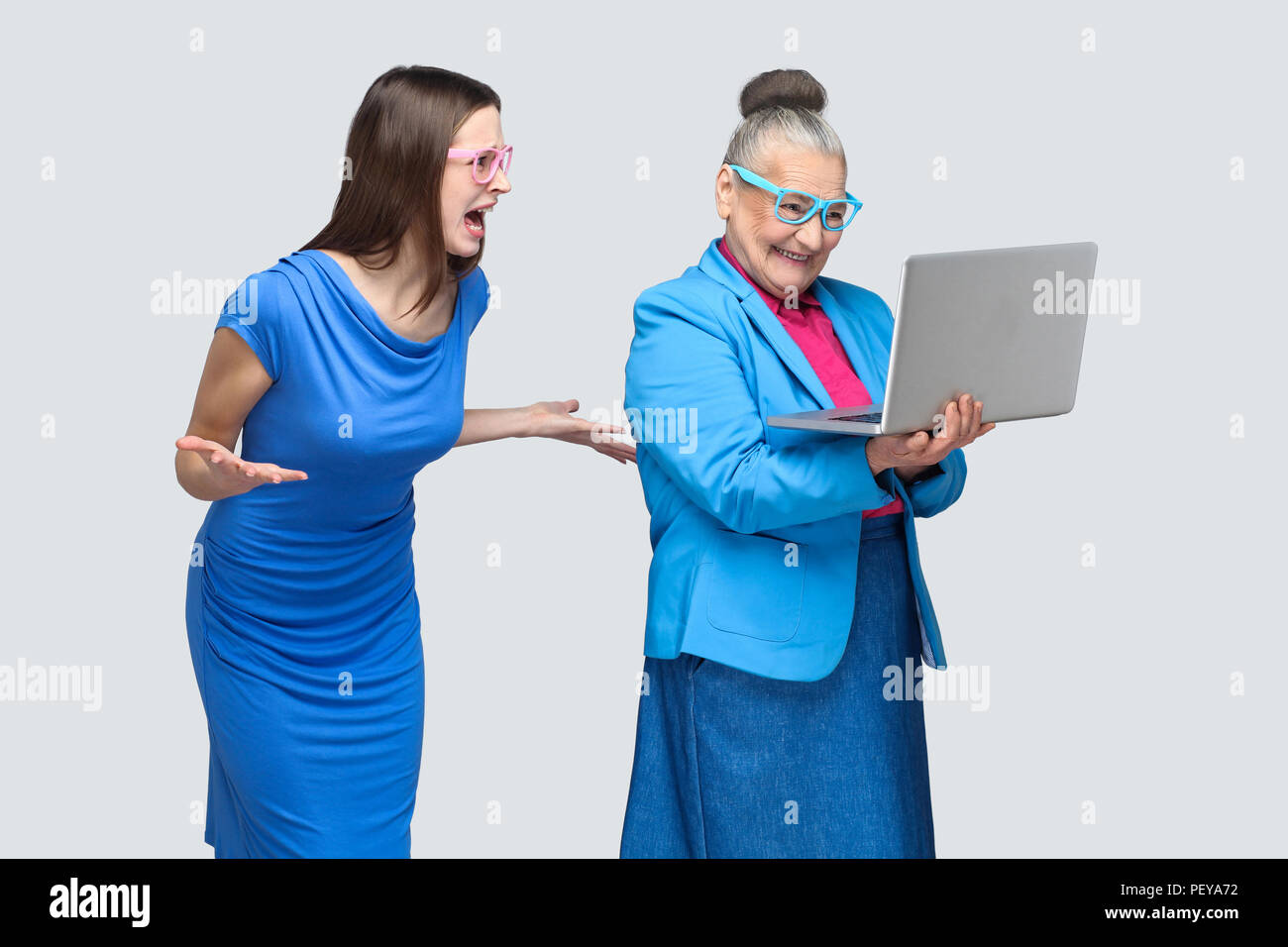 Malheureux jeune femme en robe bleue en criant à l'aged woman working on laptop. Relations internationales ou sur la relation entre la famille petite-fille et grand-mère. Banque D'Images