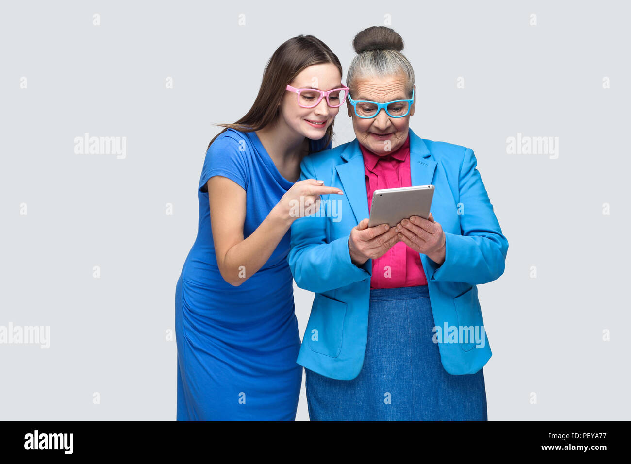Jeune fille en robe bleue, montrant du doigt l'écran de pointage tablette en mains de femme âgée. Les relations familiales entre petite-fille et grand-mère Banque D'Images