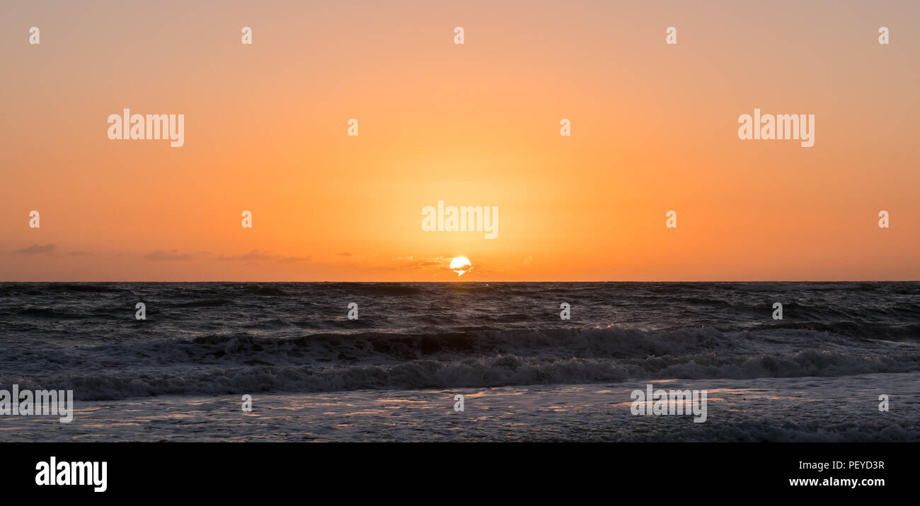 Photo de la position centrale de soleil sur une plage avec un ciel orange et rose. Banque D'Images