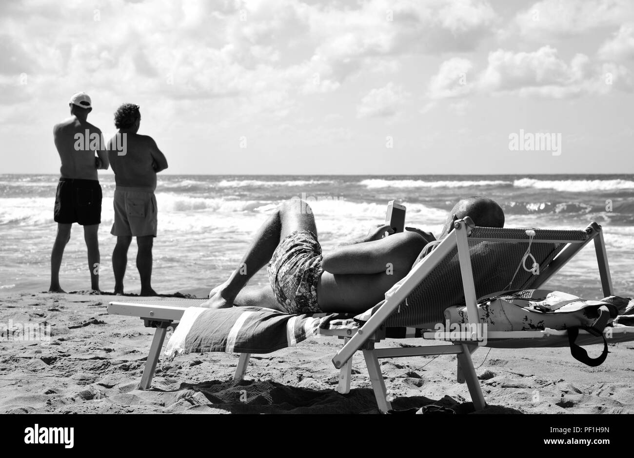 Deux types de la contemplation de notre ère technologique. Un seul homme contemple son smartphone pendant que deux amis contempler la mer infinie. Sabaudia Banque D'Images