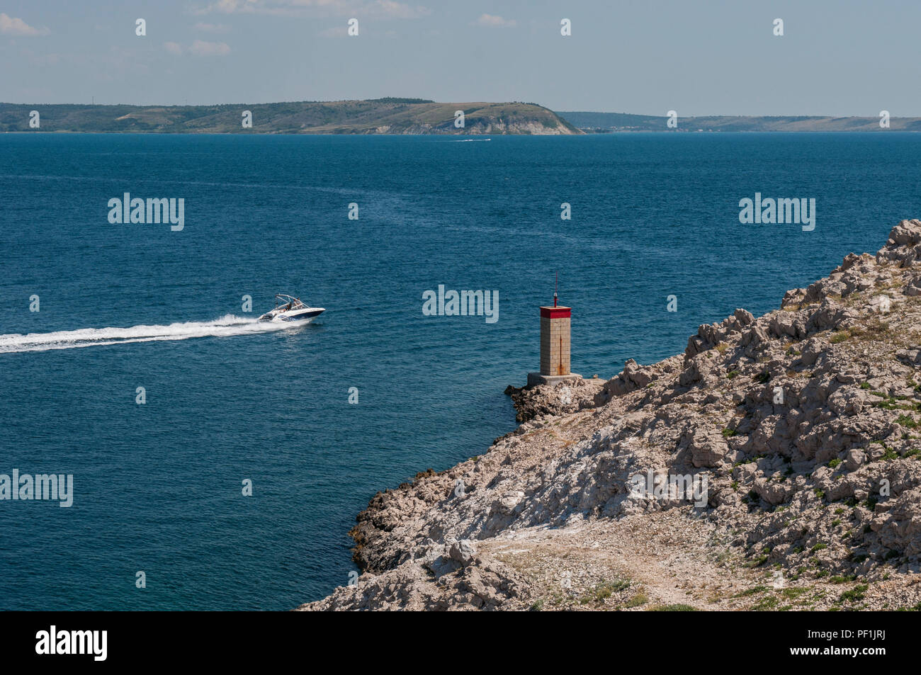 Croatie : un hors-bord et le petit phare rouge sur la falaise en face de la plus Paški, 1968 pont qui relie la terre ferme et l'île de Pag Banque D'Images