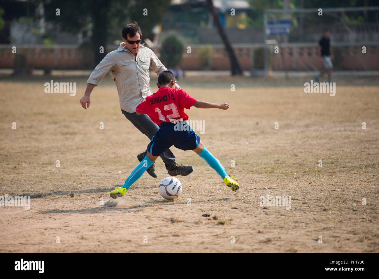 Un membre du 320e escadron de tactiques spéciales participe à un match de football avec des étudiants de l'école Nong-wha Nong-Yai pendant Cobra Gold 16 à Nam Phong, Thaïlande, le 15 février 2016. L’événement offre un engagement communautaire, renforce les relations civilo-militaires et permet au personnel du 353e SOG d’interagir avec les enfants. Des activités telles que le sport favorisent le travail d'équipe, la confiance et les relations positives entre les forces américaines et la Royal Thai Air Force au cours de cet exercice conjoint. Banque D'Images