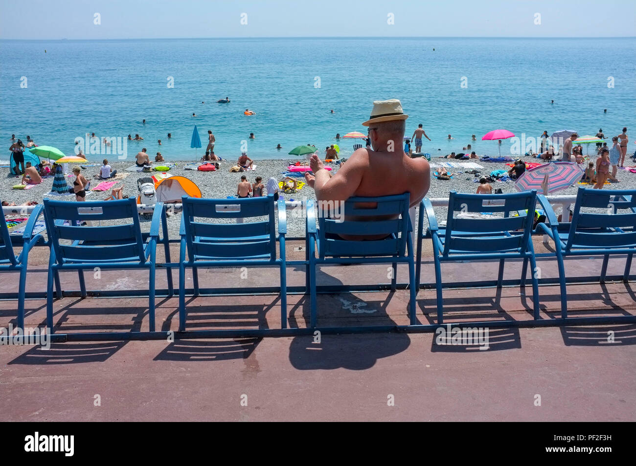 Un homme est assis sur les chaises bleues sur la Promenade des Anglais à  Nice France et regarde les amateurs de plage Photo Stock - Alamy