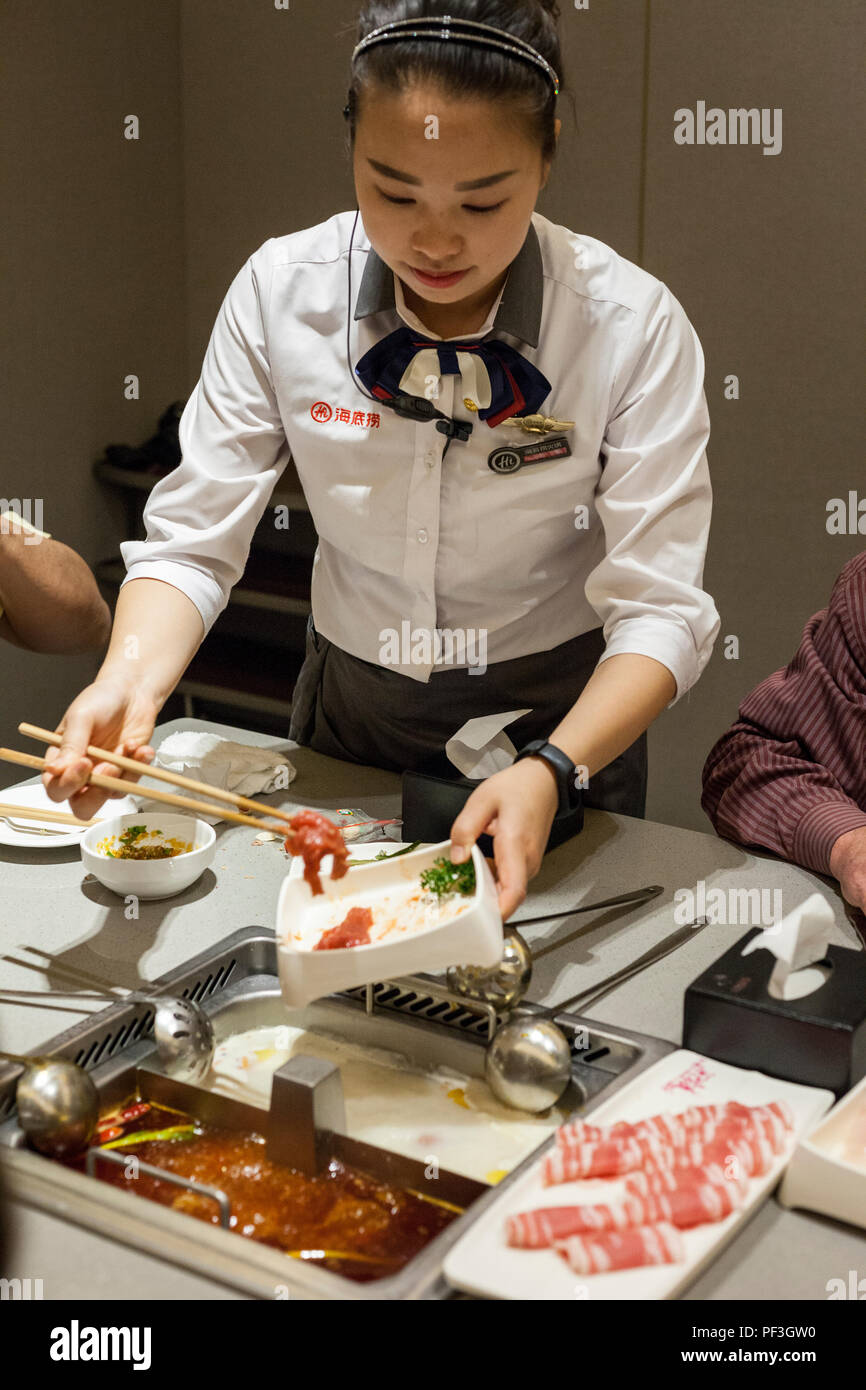 Nanjing, Jiangsu, Chine. Serveuse en plaçant le boeuf dans une marmite pour la cuisson à table. Restaurant Haidilao. Banque D'Images Nanjing, Jiangsu, Chine. Serveuse en plaçant le boeuf dans une marmite pour la cuisson à table. Restaurant Haidilao. Banque D'Images