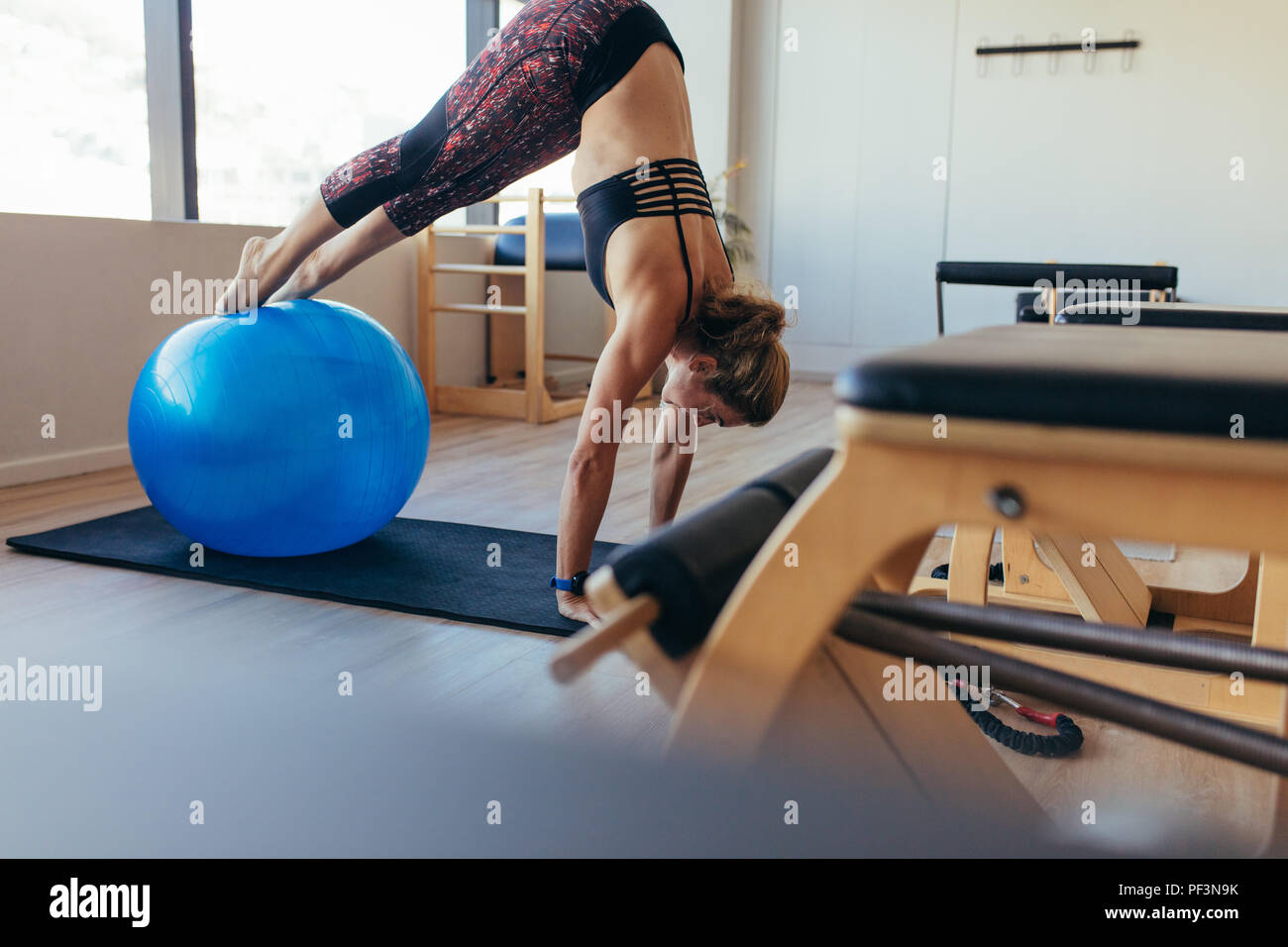 Formation femme avec une balle de remise en forme à la salle de sport. Femme en position push up avec pieds reposant sur une boule d'exercice à un gym pilates. Banque D'Images