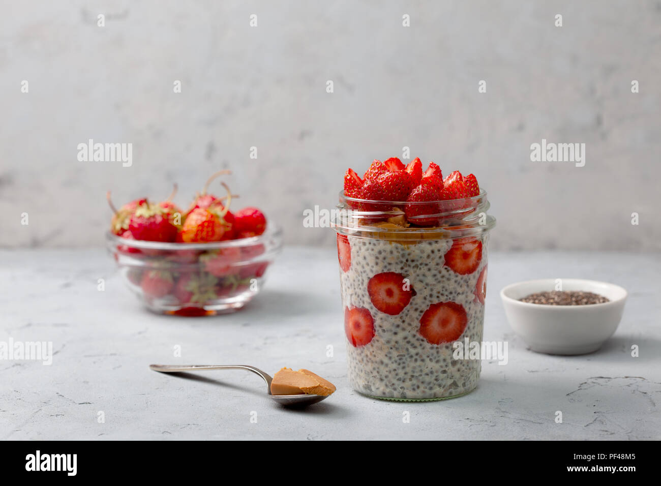 Petit-déjeuner sain. nuit du gruau avec des fraises, chia graines dans un bocal de verre sur fond gris Banque D'Images