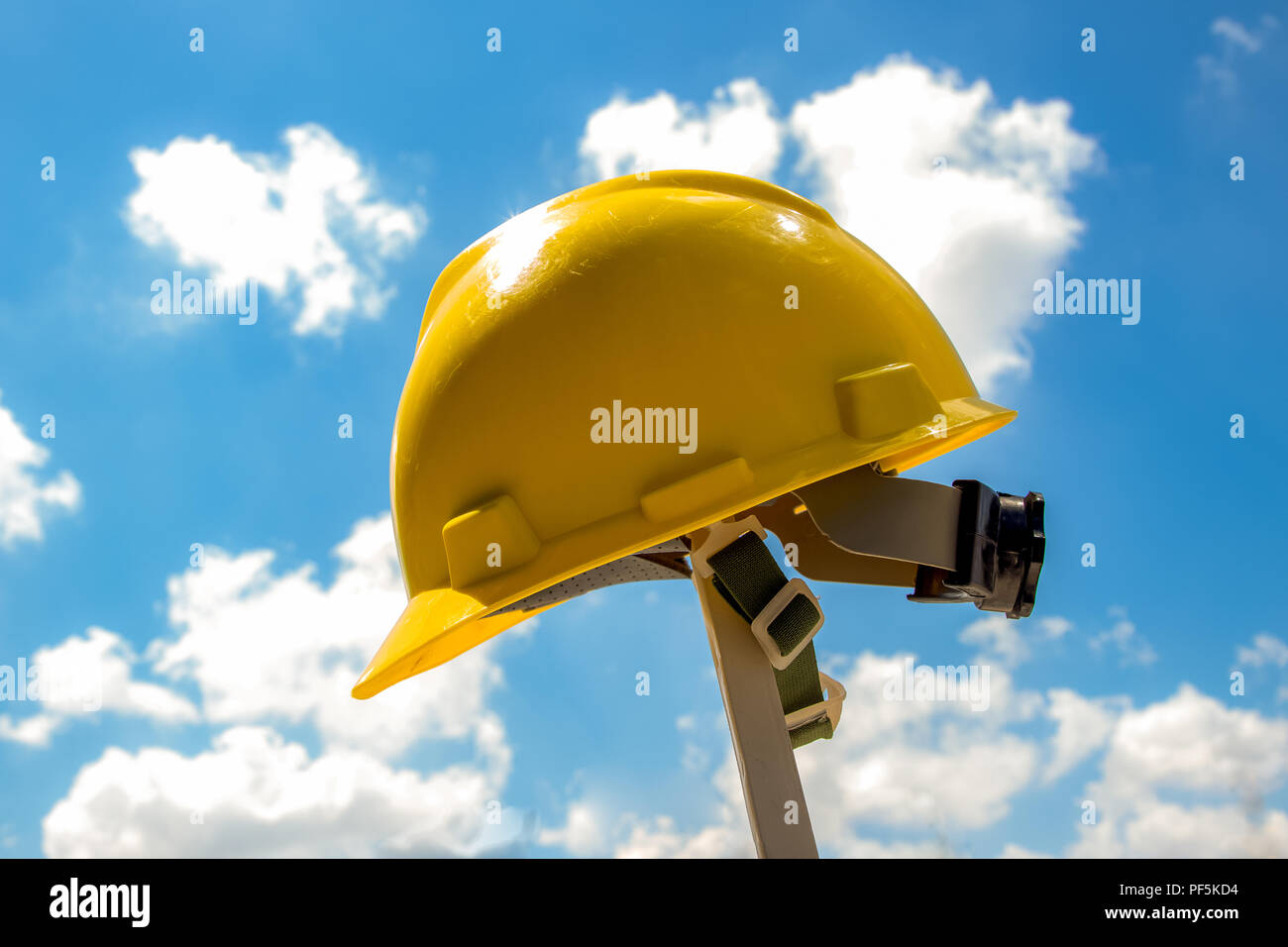 Casque de protection jaune pendu à un poteau sur un chantier de construction sous un soleil éclatant contre un ciel nuageux ciel bleu Banque D'Images