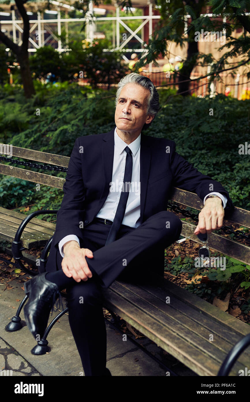 L'homme aux cheveux gris en costume noir est assis sur banc de parc Banque D'Images