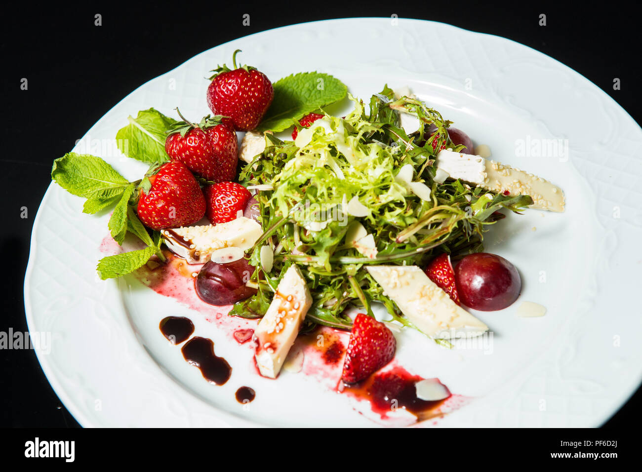 Avec salade de cerise, de fraise et fromage sur un grand plat blanc sur fond noir Banque D'Images