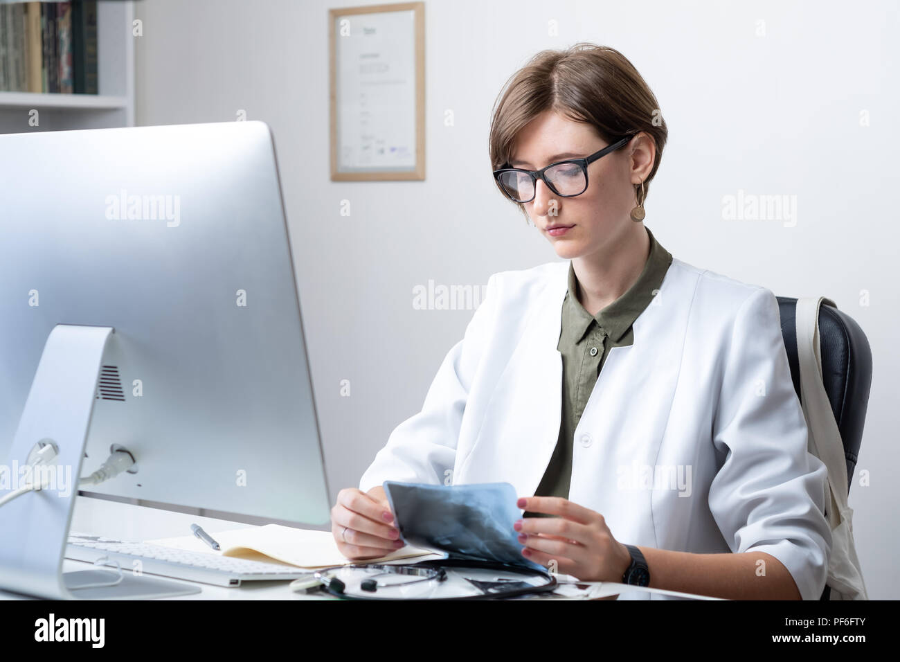Femme médecin à médecin moderne bureau. Femme praticienne examining x-ray sur le lieu de travail devant un ordinateur de bureau Banque D'Images