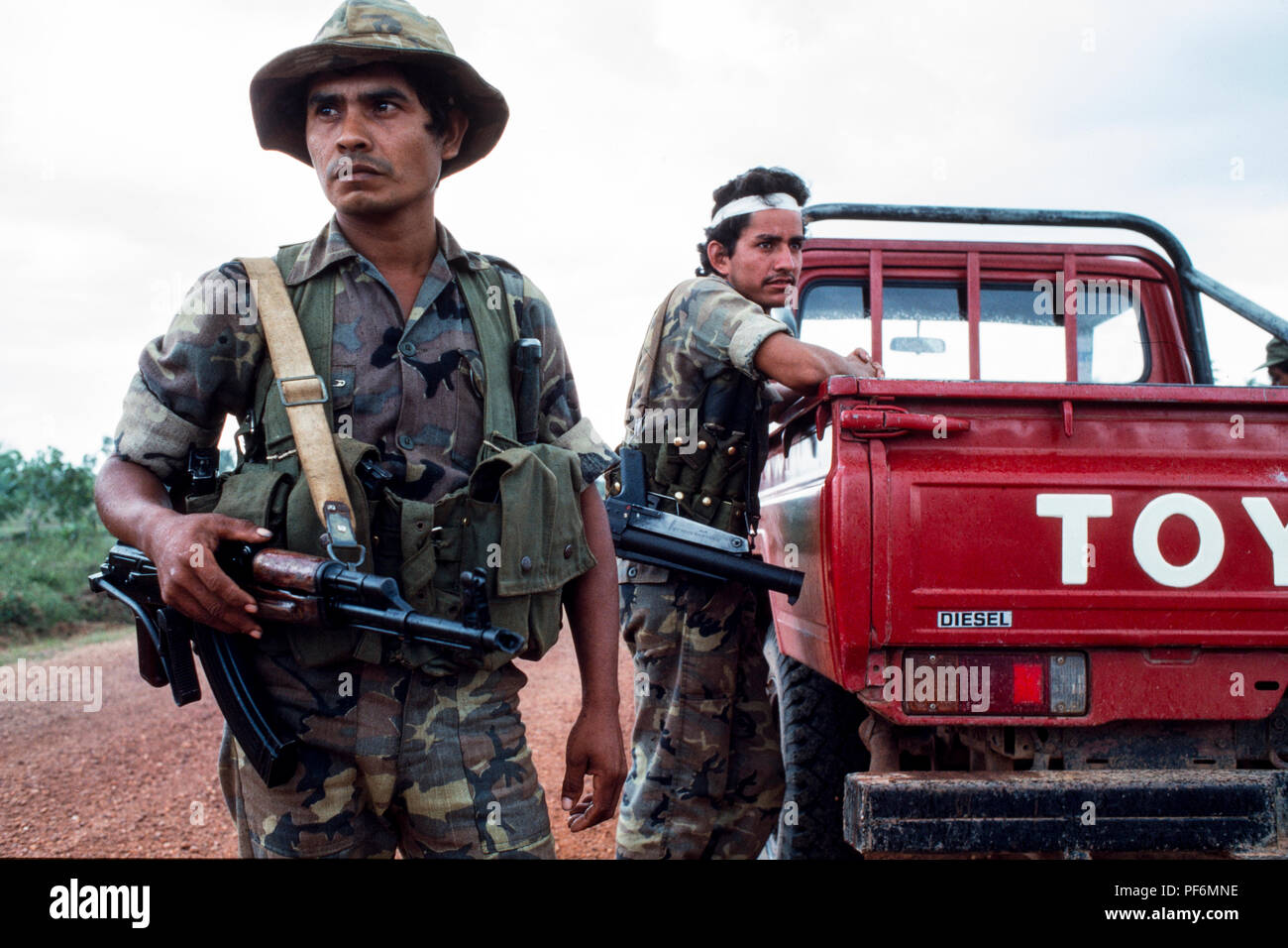 Deux soldats armés en uniformes de camouflage à côté d'un camion Toyota rouge sur un chemin de terre. Banque D'Images