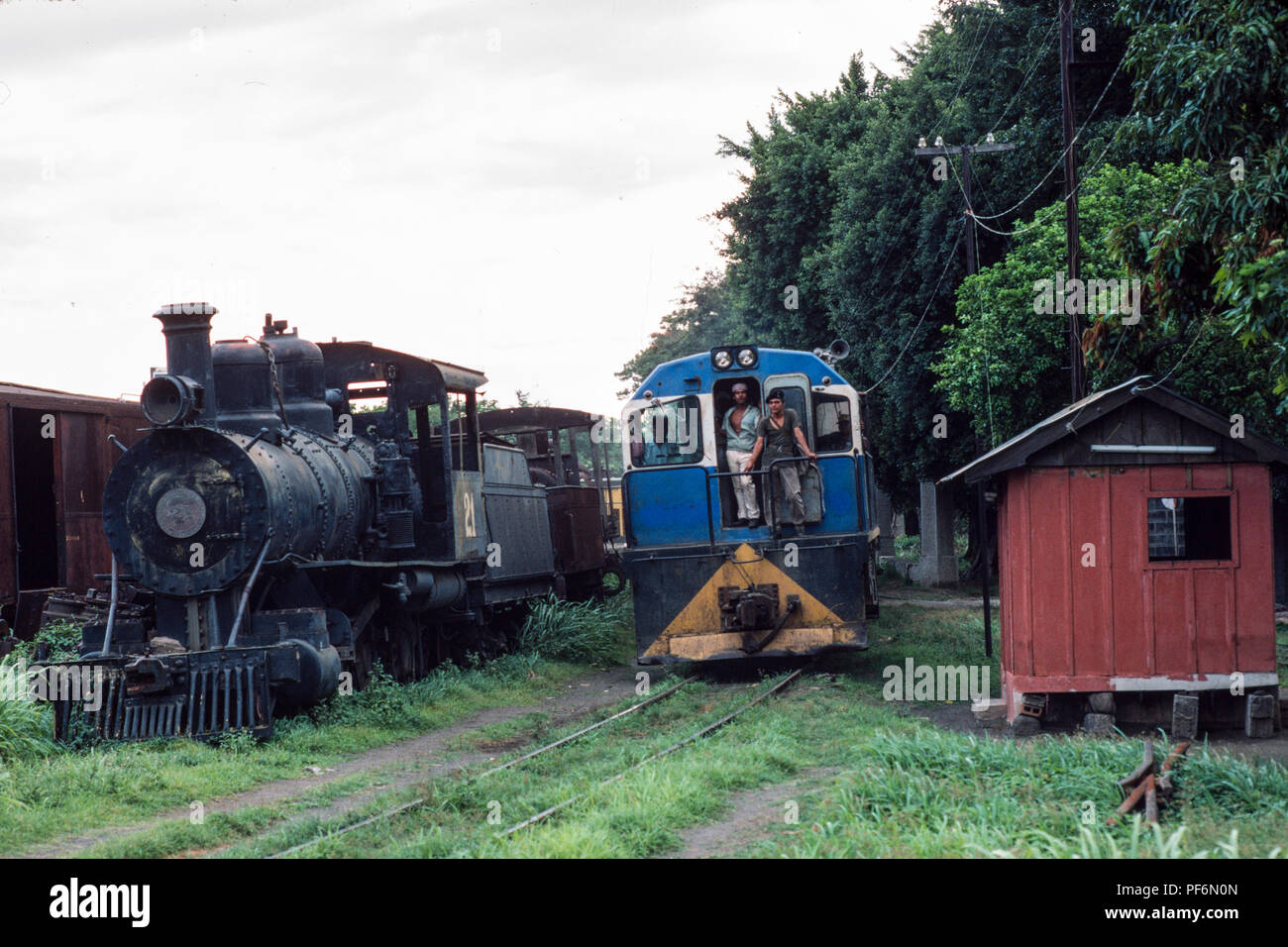 Managua, Nicaragua, 12 février 1990, un train de marchandises par chemin de fer gare de disques dans Managua, passé sur la vieille machine à vapeur abandonnés stationné dans un garage. Banque D'Images