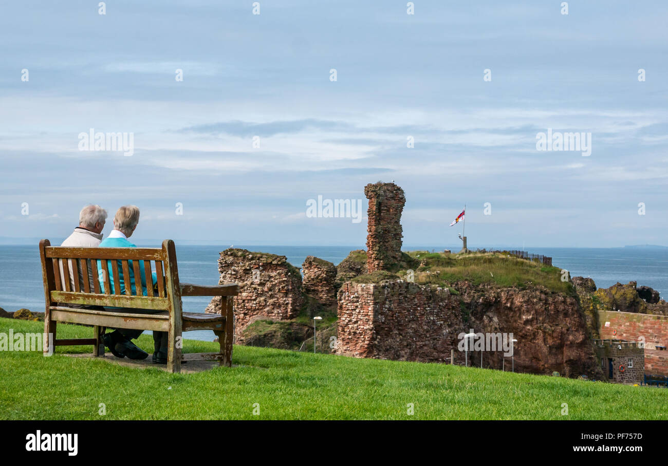 Dunbar, East Lothian, Ecosse, Royaume-Uni, 20 août 2018. UK Soleil dans le port de Dunbar. Un vieux couple profiter du soleil assis sur un banc au-dessus du port, en vue de l'enceinte du château de Dunbar Banque D'Images