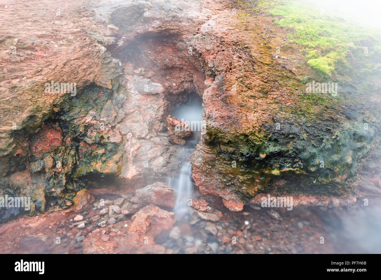 Gros plan du geyser de vapeur à Deildartunguhver hot springs en Islande avec brouillard brouillard nuageux long sortant de l'exposition rock rouge grotte colorée ébullition Banque D'Images