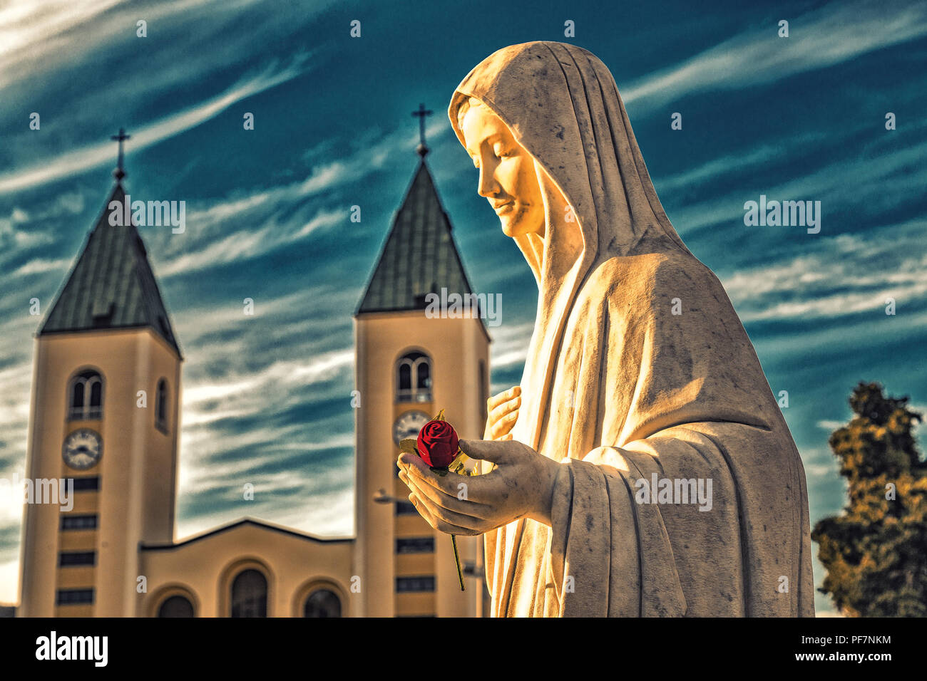 Statue de la Vierge Marie tenant une rose rouge alors que l'église Saint Jacques de Medjugorje est en arrière-plan Banque D'Images