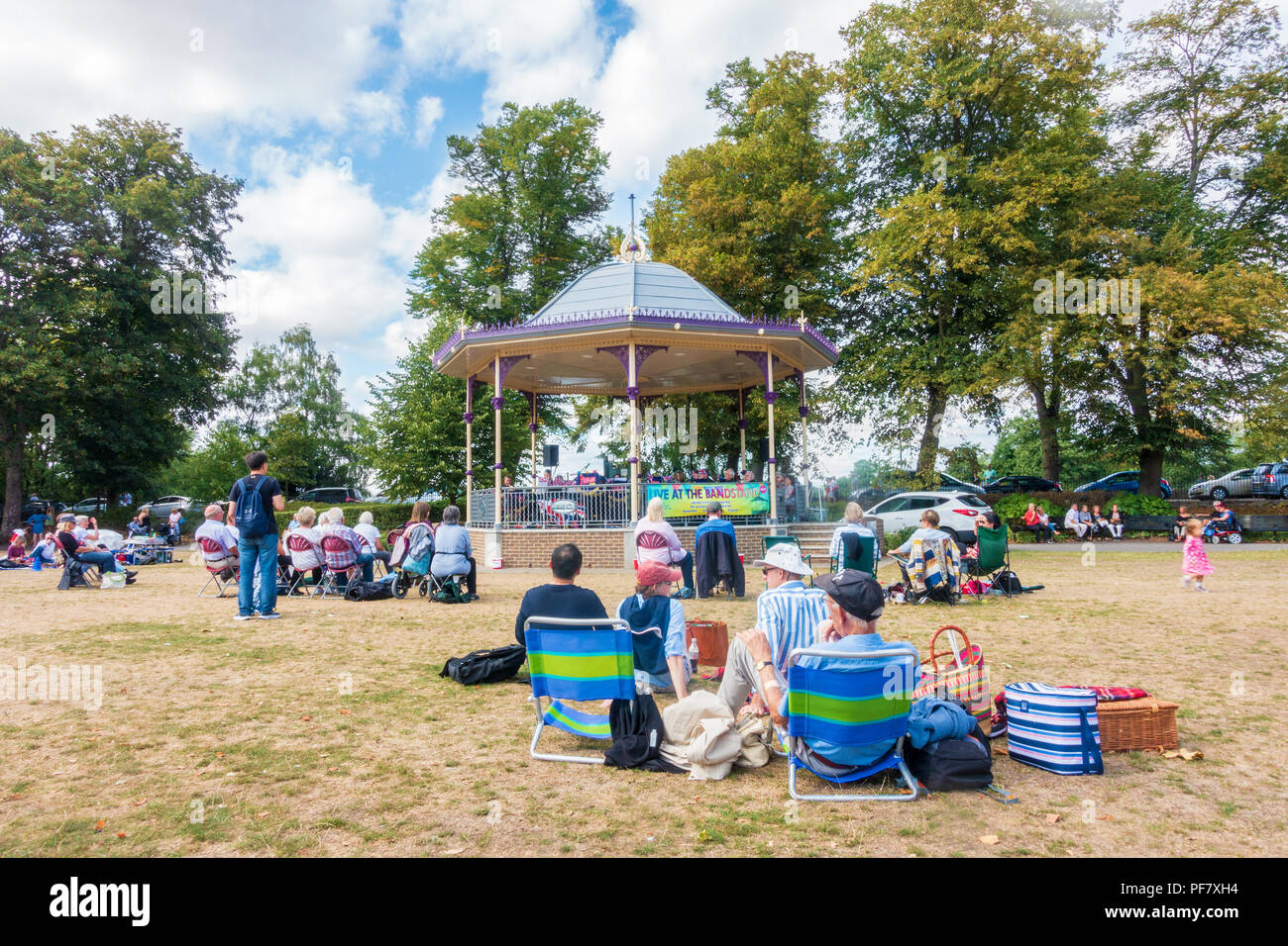 Un groupe joue un concert gratuit dans la région de band stand Alexandra Gardens à Windsor, Royaume-Uni. Les gens s'assoient sur des chaises pliantes, benchses et le sol à regarder. Banque D'Images