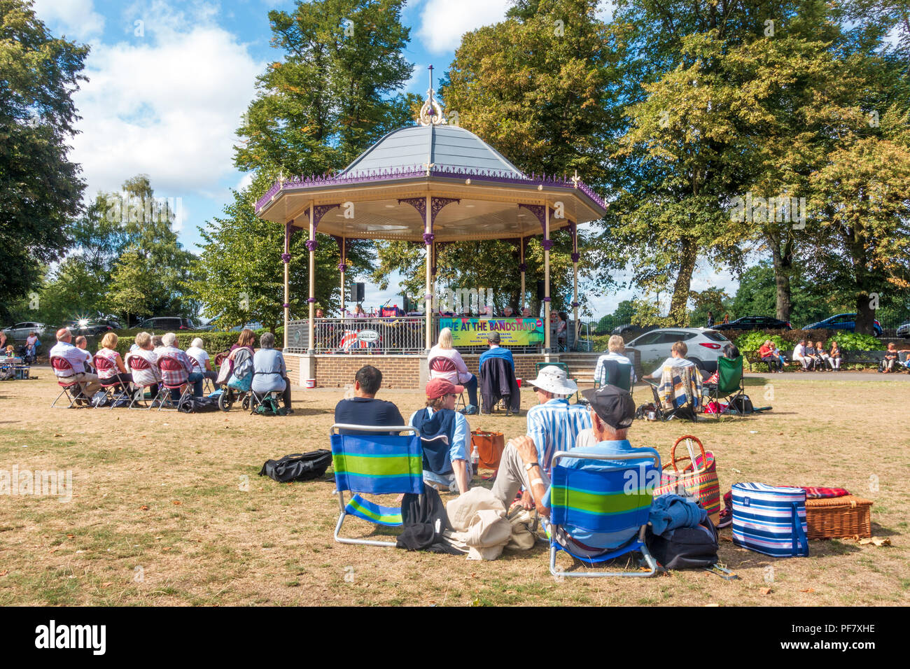 Un groupe joue un concert gratuit dans la région de band stand Alexandra Gardens à Windsor, Royaume-Uni. Les gens s'assoient sur des chaises pliantes, benchses et le sol à regarder. Banque D'Images