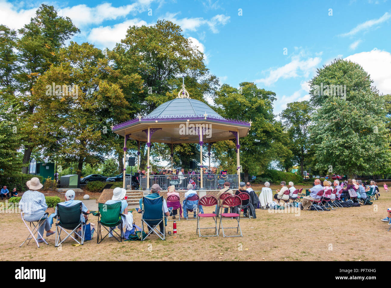 Un groupe joue un concert gratuit dans la région de band stand Alexandra Gardens à Windsor, Royaume-Uni. Les gens s'assoient sur des chaises pliantes, benchses et le sol à regarder. Banque D'Images