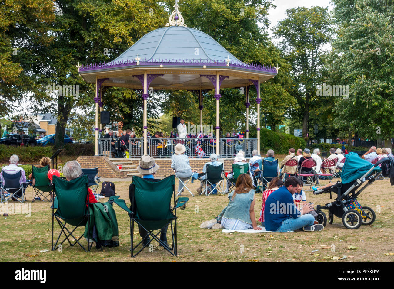Un groupe joue un concert gratuit dans la région de band stand Alexandra Gardens à Windsor, Royaume-Uni. Les gens s'assoient sur des chaises pliantes, benchses et le sol à regarder. Banque D'Images