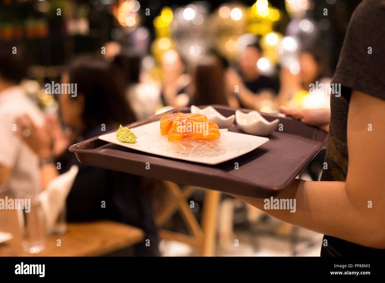 Franc tourné en haute iso avec faible lumière waitress serving salmon sashimi à client en restaurant Banque D'Images