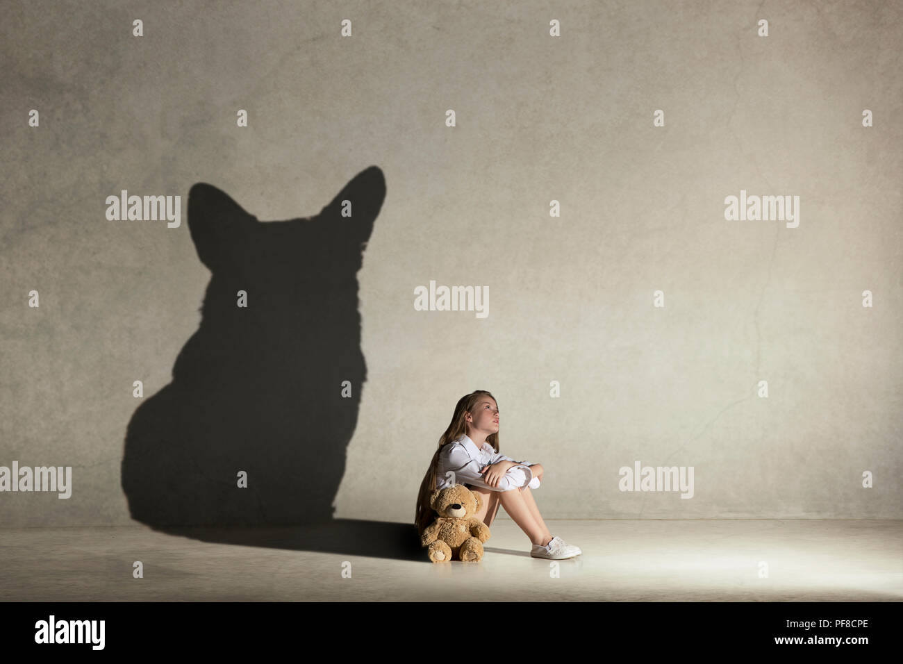 Petite fille à rêver de chien. L'enfance et de l'dream concept. Image conceptuelle avec l'ombre de femme figure sur le mur de studio Banque D'Images
