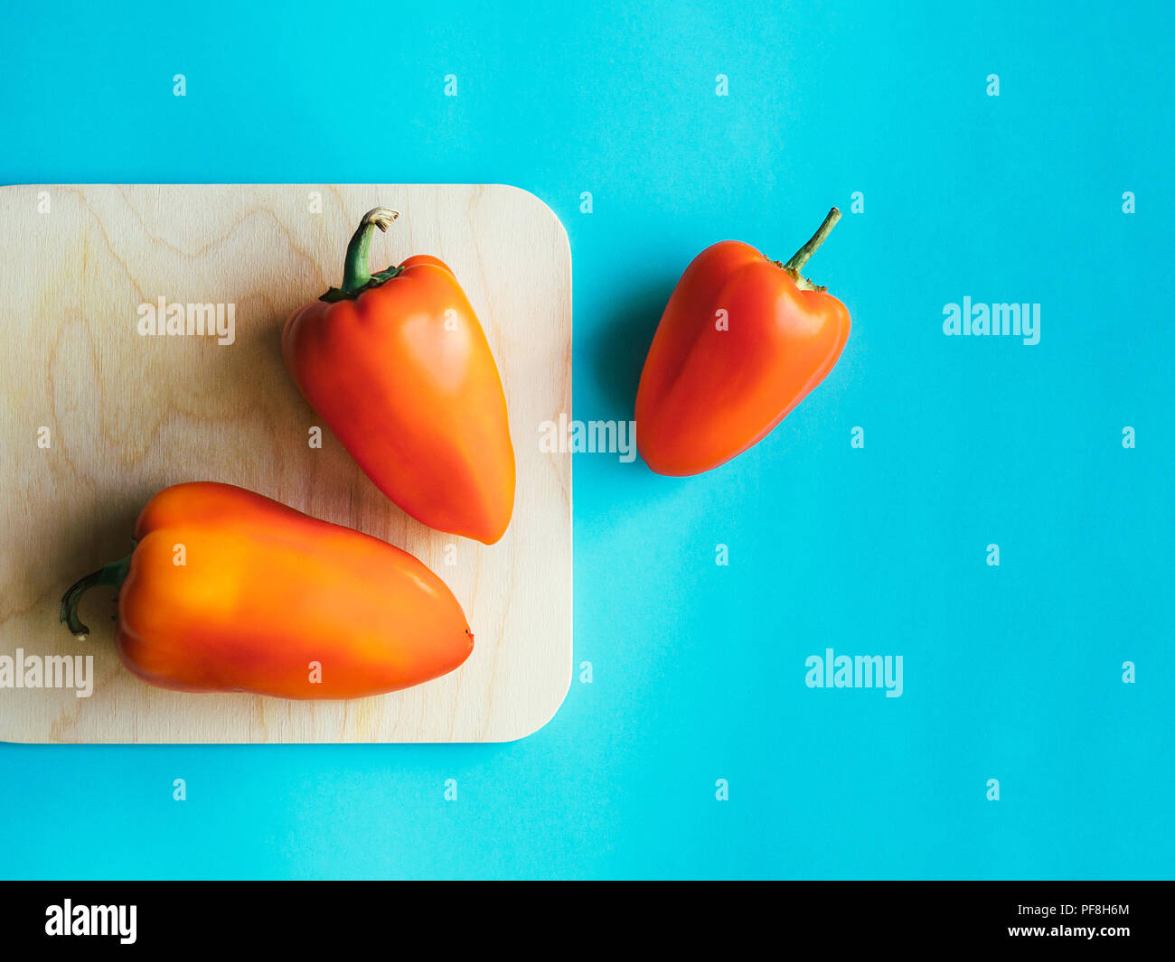 Haut de poivre voir trois gros poivrons rouges sont situées sur une planche à découper sur un fond bleu Banque D'Images