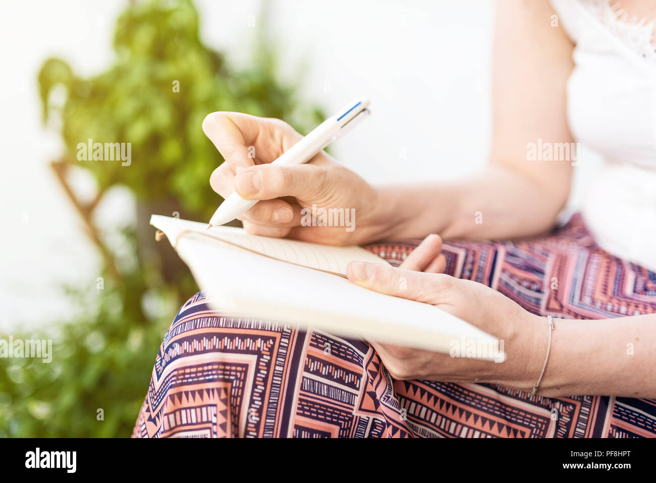 Femme assise sur le patio en prenant des notes dans l'ordinateur portable Banque D'Images