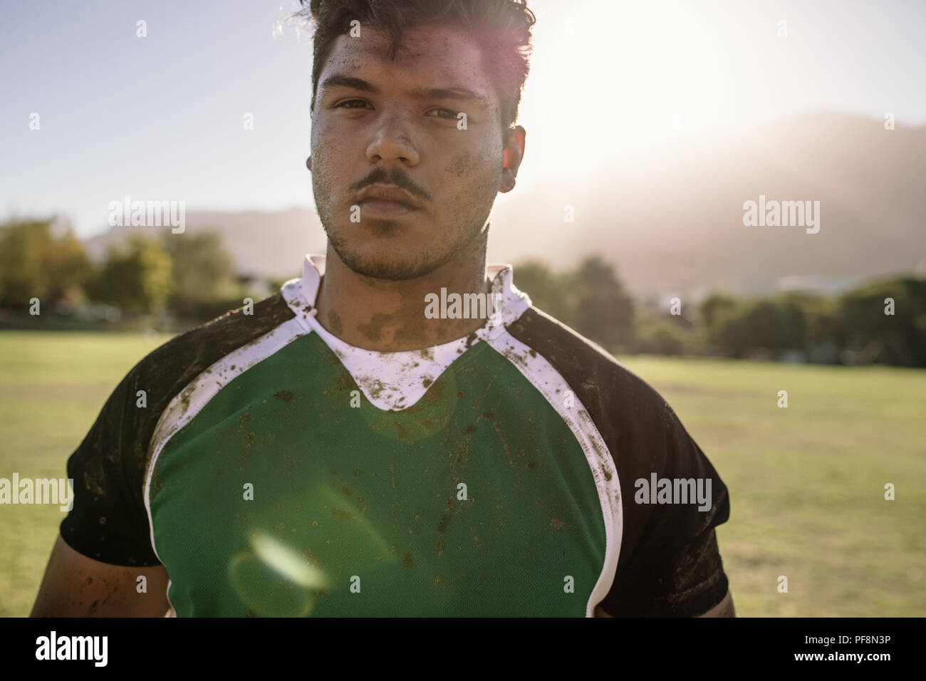 joueur de rugby sur le terrain de sport. Jeune sportif avec le visage et uniforme enduit dans la boue avec la lumière du soleil brillant. Banque D'Images