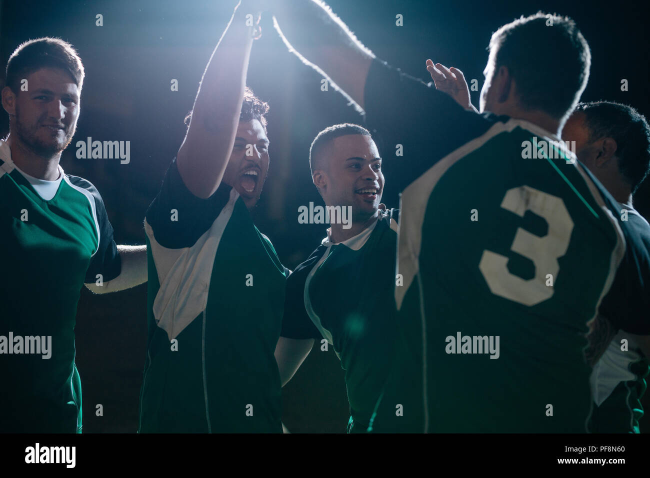 joueurs de rugby célébrant un but sur le terrain de sport. équipe de rugby avec les mains levées et criant après avoir marqué sous les lumières. Banque D'Images