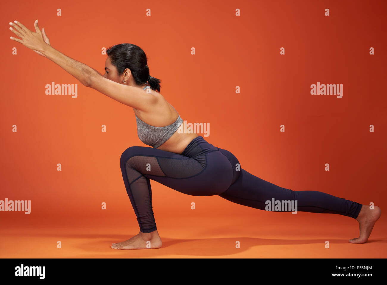 Fente en croissant vers l'yoga pose woman show sur fond de couleur orange studio Banque D'Images